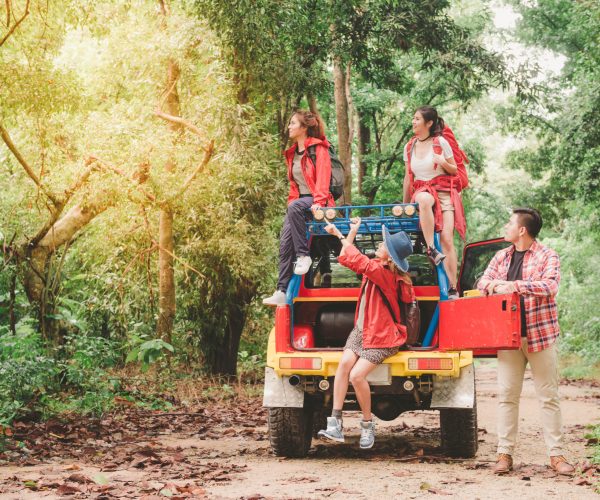 Happy asian young travellers with 4WD drive car off road in forest, young couple looking for directions on the map and another two are enjoying on 4WD drive car. Young mixed race Asian woman and man.