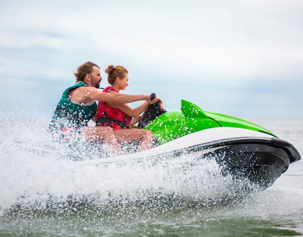 young people having fun driving on high speed on water scooter, man and woman on summer vacation, friends doing active sport