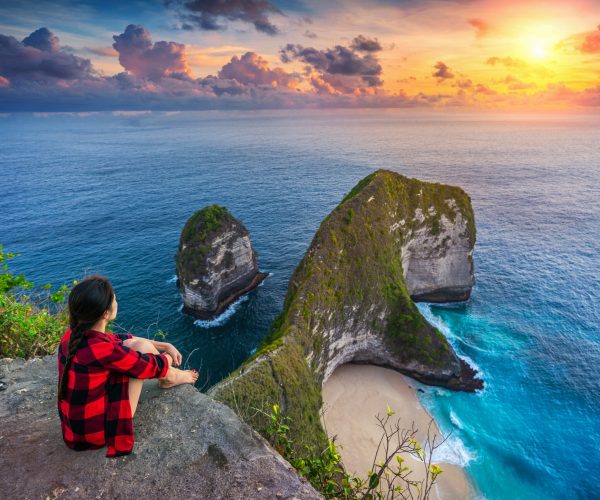 Woman sitting on cliff and looking at sunset at Kelingking Beach in Nusa penida island, Bali, Indonesia.