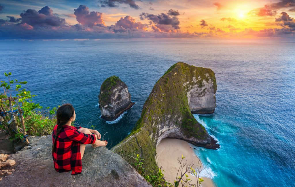 Woman sitting on cliff and looking at sunset at Kelingking Beach in Nusa penida island, Bali, Indonesia.