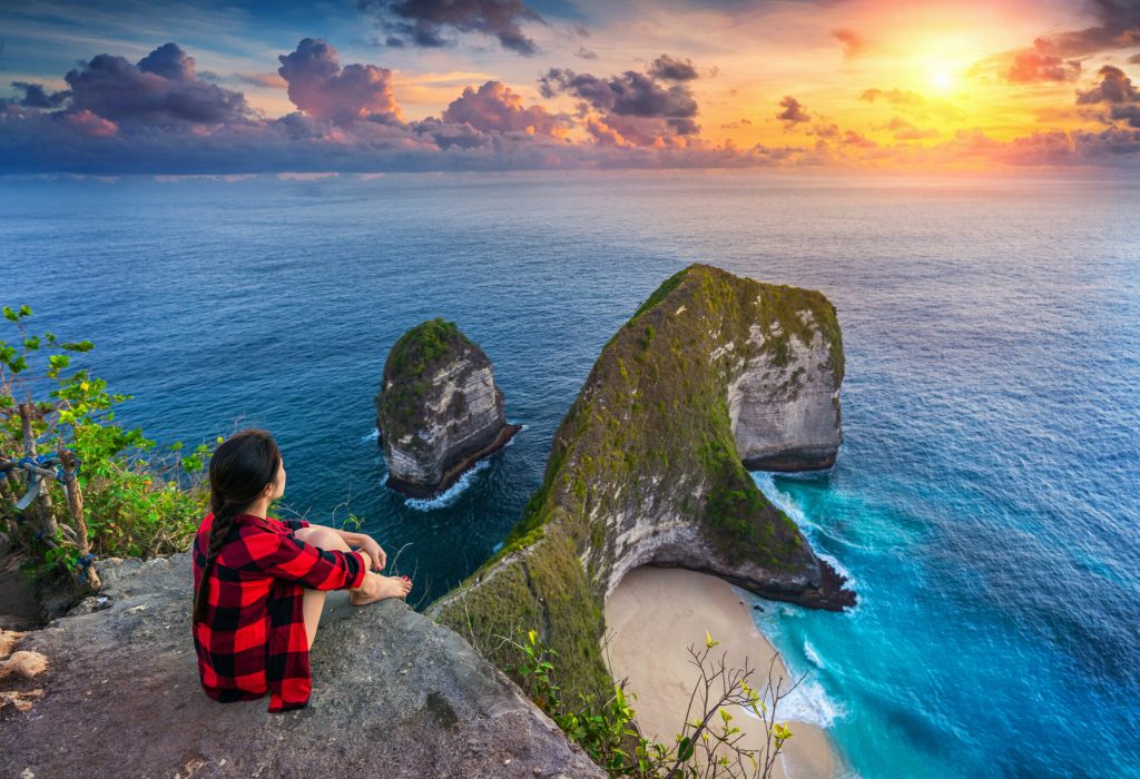 Woman sitting on cliff and looking at sunset at Kelingking Beach in Nusa penida island, Bali, Indonesia.