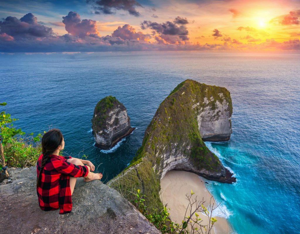 Woman sitting on cliff and looking at sunset at Kelingking Beach in Nusa penida island, Bali, Indonesia.